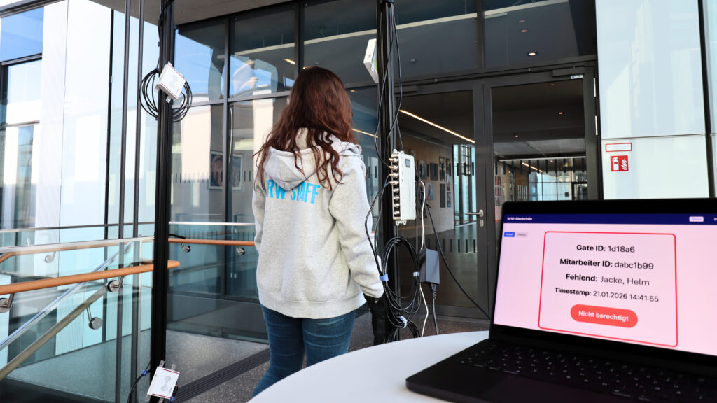 Man sieht eine Frau in einem grauen Hoodie durch ein Gate laufen. Ein Laptop im Vordergrund zeigt an, dass sie keine Berechtigung hat einzutreten.